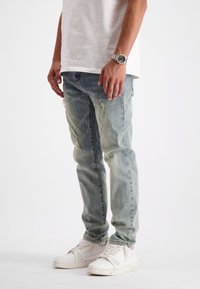  Lichtblauwe distressed jeans met een slim fit, met scheurranden en een vervaagde wassing, gecombineerd met witte sneakers en een casual wit shirt.