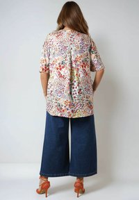 Floral blouse in pastel colors with short sleeves, paired with wide-leg dark denim pants. The outfit is complemented by orange heeled sandals.