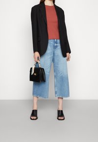 Černý oversize blejzr, top v cihlové barvě, světle modré široké džíny, černé otevřené muly a malá černá kabelka s vzorovaným popruhem.