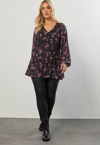 Blusa nera a fiori con maniche lunghe trasparenti e scollatura a V. Abbinata a leggings neri e stivaletti, creando una silhouette a strati.