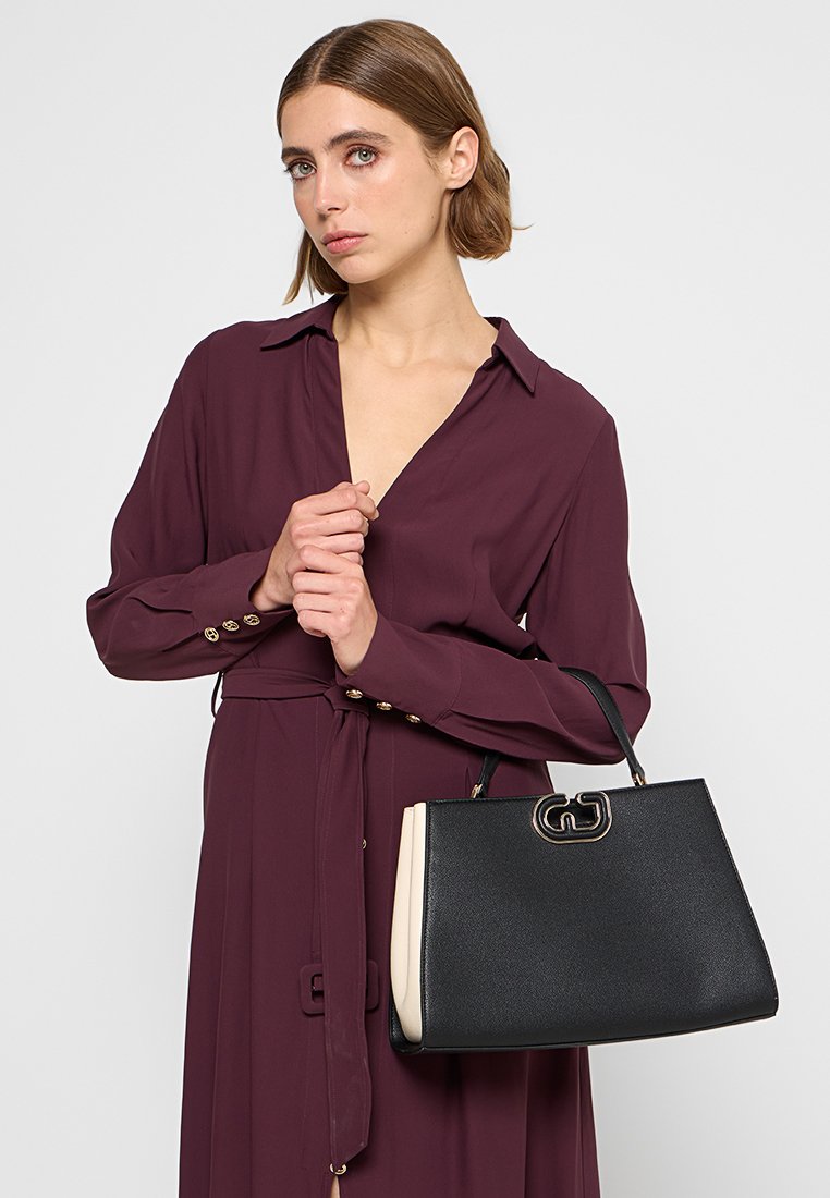 Borsa strutturata nera e crema con superficie texturizzata, accessori in oro e un logo di grandi dimensioni sul davanti.