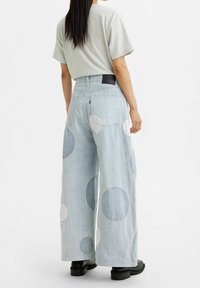 Pantalones de mezclilla de pierna ancha en azul claro con grandes parches circulares en diferentes tamaños en blanco y azul oscuro. Presenta una cintura estándar y bolsillos traseros.