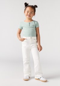Une chemise courte à manches courtes couleur vert clair à côtes avec des détails de bouton, associée à un jean blanc évasé et des baskets blanches avec des accents verts.