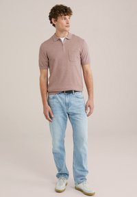 Polo shirt cu mânecă scurtă, de culoare roz deschis, cu fermoar și buzunar, purtat cu blugi de denim bleu și adidași albi. Îmbrăcăminte casual.