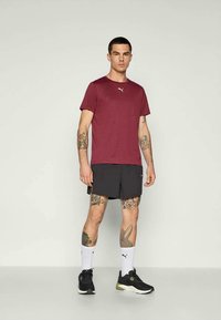 Körsbärsröd tränings T-shirt med rund halsringning, kombinerad med svarta shorts. Har Puma-logotyp på bröstet, bärs med vita strumpor och svarta sneakers.