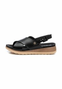 Sandalo in pelle nera con cinturini incrociati, cinturino posteriore regolabile e suola beige texturizzata. Presenta un logo discreto sul lato.