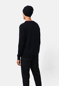 Donkerblauwe trui met een geribbelde onderrand en manchetten, gemaakt van een zacht materiaal. Gecombineerd met een bijpassende beanie, in een ontspannen pasvorm gestyled.