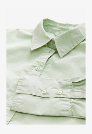 Hellgrünes Hemd mit spitzem Kragen, zwei vorderen Knöpfen und glatter Textur. Hat einen umgeschlagenen Ärmeln mit Knopfdetails.