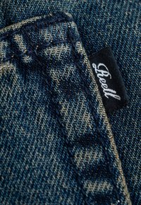 Blauer Denim-Stoff mit sichtbarem Webmuster, versehen mit einem schwarzen Etikett mit weißem Text, das in die Naht genäht ist.
