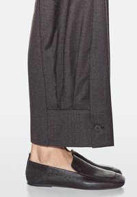 Chaussures noires sans lacets associées à un pantalon gris taillé avec revers et détail de bouton, fabriqué dans un tissu texturé.