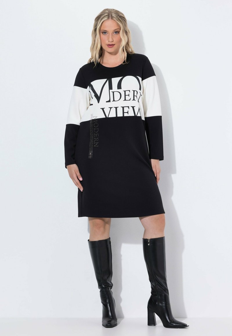 Schwarz-weißes Langarmkleid mit grafischem Text "MODERN VIEW", kombiniert mit hochhackigen schwarzen Lederstiefeln. Glattes Material, lässige Passform.