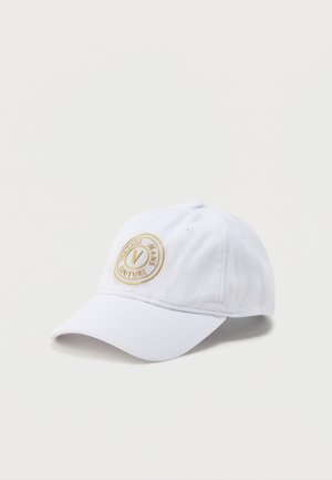 Cappellino da baseball bianco con visiera curva e toppa rotonda beige con logo riportante la scritta "Versace Jeans Couture" sul pannello frontale.