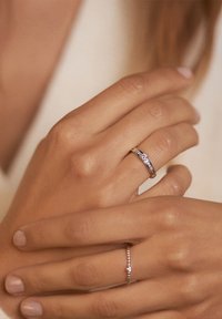 Silberringe, die an Fingern getragen werden; einer hat ein strukturiertes Band mit Edelsteinen, der andere ein Perlenmuster. Helle Hautfarbe, unlackierte Nägel.