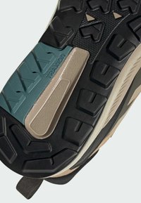 Športové topánky majú textúrovanú čiernu gumovú podrážku s tyrkysovou a béžovou medzipodrážkou, ktorá zobrazuje dynamický vzor trakcie.