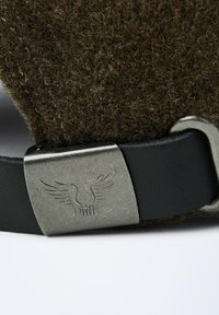Gros plan d'un tissu en laine sombre avec une sangle en cuir noir et un fermoir en métal brossé portant un logo à ailes gravé.