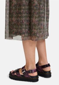 Zwarte en paarse sandalen met bandjes en gespen, met een textuur bovenwerk en een dikke rubberen zool. Draagt een geplooide, patroon, semi-doorzichtige rok.
