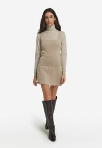 Beżowa dzianinowa sukienka z kwadratowym dekoltem, noszona na jasnoszarym golfie. Dobranie do wysokich, ciemnobrązowych, dopasowanych kozaków. Gładka faktura.