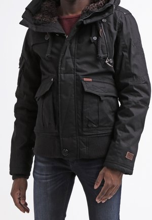 Sort dunjakke med hætte, foret med imiteret pels, flere lommer foran og ribbet kant. Materialet ser ud til at være vandafvisende.