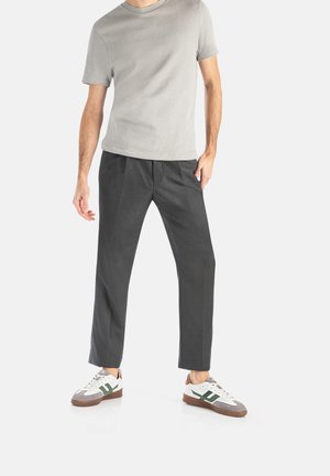 T-shirt grigio a maniche corte abbinato a pantaloni scuri e sneaker bianche con accenti verdi. Il tessuto appare liscio e strutturato.