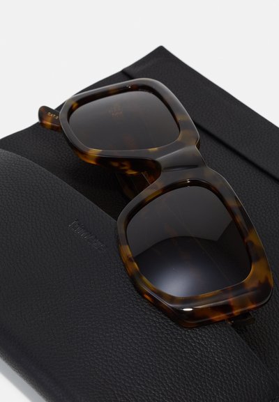 Tortoiseshell sunglasses with large square frames and dark lenses, resting on a textured black leather case.
