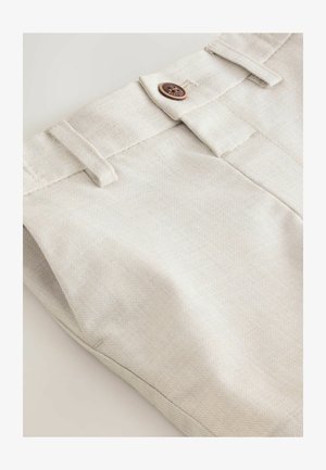 Bézs pamut nadrág texturált felülettel, barna gombbal és két övbújtatóval a derékrészen. Nyers szegély részlet látható.