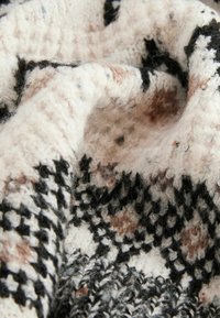 Texturerat stickat tyg i kräm, svart och ljusbrunt, med ett geometriskt mönster som har variationer i tjocklek och fuzzy fibrer.