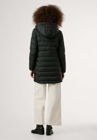 Zwarte pufferjas met capuchon, voorzien van doorgestikte design en zijzakken, gecombineerd met witte wijde broek en zwarte hakken tot de enkel.