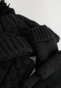 Schwarzes, gestricktes Winteraccessoires-Set bestehend aus einer Mütze mit Pompon, fingerlosen Handschuhen und einem Schal mit strukturierten Mustern.