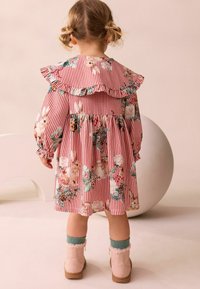 Rot-weißer gestreifter Kleid mit Blumenmustern, die Hasen zeigen, einem gefransten Kragen und langen Ärmeln. Beige Knöchelstiefel mit fellbesetzten Akzenten.