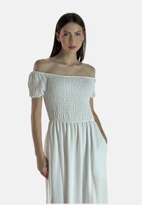 Off-the-shoulder hvid kjole med korte puffærmer, der har et smocket liv og en flowy nederdel, lavet af let materiale.