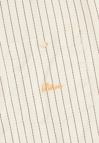 Lys cremet skjorte med tynde brune striber, featuring en brystlomme og en beige knap, prydet med "Blkoi" broderet i orange.
