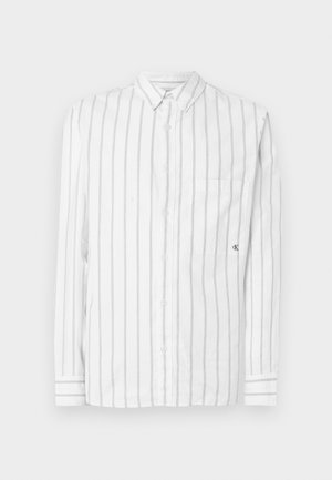 Camisa branca de manga comprida com finas riscas verticais cinzentas, gola com botões, bolso frontal único e logótipo CK no bolso.