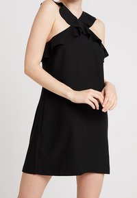 Abito nero senza maniche con scollo arricciato e silhouette leggermente a trapezio; texture del tessuto liscia; senza chiusure o modelli visibili.