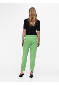 Pantalon vert à taille élastique, coupe droite, poches latérales et texture lisse, associé à un haut noir à manches courtes.