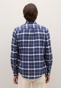Marineblaue und weiße karierte Langarmbluse mit Knöpfen, abgerundetem Saum und Passe; aus gewebter Baumwolle für eine strukturierte Optik gefertigt.