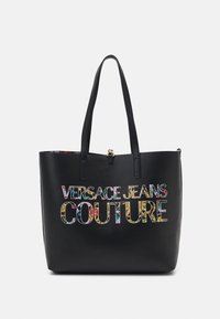 Černá taška přes rameno z umělé kůže s logem "VERSACE JEANS COUTURE" v barevném květinovém potisku. Dva pevn é držadla a horní zipové uzavření.