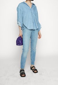 Ljusblå denimskjorta med lång ärm och avslappnad passform, matchad med ljusblå jeans. Accessoarer inkluderar en liten lila väska och svarta sandaler.