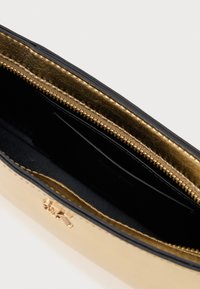 Χρυσό μεταλλικό τσαντάκι με μαύρες λεπτομέρειες, λεία υφή, κλείσιμο με φερμουάρ και μαύρο εσωτερικό που διαθέτει θήκη για κάρτα και λεπτομέρεια με λογότυπο.