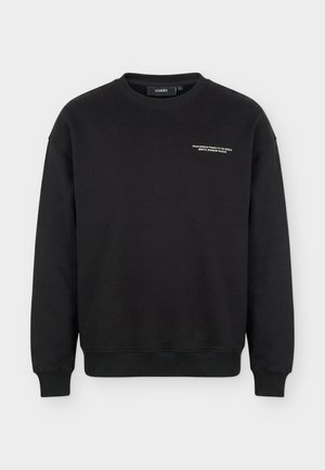 Μαύρο φούτερ με μακριά μανίκια και στρογγυλή λαιμόκοψη, με μικρό λευκό κείμενο στο αριστερό μέρος του στήθους που γράφει "From Fabrica Franco to the World Benetica Driven by Passion."