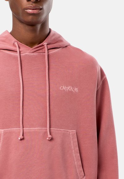 Rosa hoodie med ficka fram, kontrasterande sömmar och broderad "CAMPERLAB" logotyp på bröstet. Tyget ser mjukt och strukturerat ut.
