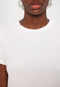 Λευκό βαμβακερό μπλουζάκι με κλασικό στρογγυλό λαιμό και κοντά μανίκια, λεία υφή και ελάχιστες ραφές.