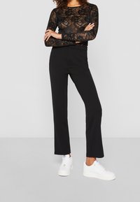 Black lace long-sleeve top with floral pattern, paired with high-waisted black trousers and white sneakers. Simple straight-leg design.