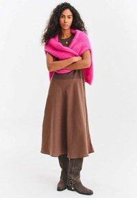 Brązowa sukienka bez rękawów o rozkloszowanym kroju, zestawiona z różowym, puszystym szalem i szarymi kozakami za kolano z metalowymi ozdobami.