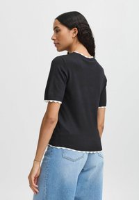 Marineblå kortærmet sweater med bølget hvid kant ved krave og ærmer, tætsiddende design og struktureret strikket materiale, parret med lyse denim jeans.