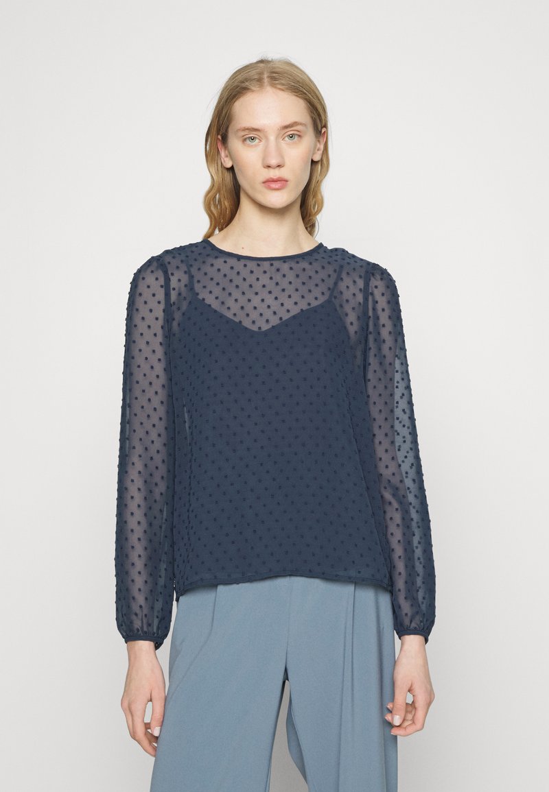 Blusa transparente azul-marinho com mangas longas e bufantes, apresentando bolinhas texturizadas e um decote arredondado. Tecido suave e leve, com um corte relaxado.