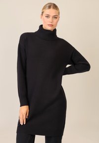 Schwarzer Strickrollkragensweater mit langen Ärmeln, geripptem Saum und lockerer Passform, der eine sanfte Textur und ein minimales Design aufweist.