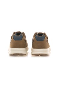 Zapatillas marrones con un acabado suave, detalles de tela azul, suelas de goma blanca y un lazo trasero para facilitar su colocación. Diseño elegante y minimalista.