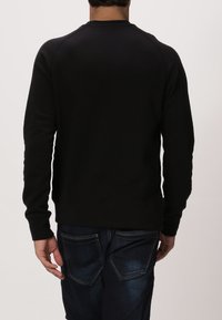 Černá mikina s kulatým výstřihem a raglánovými rukávy. Vyrobena z hladkého materiálu, má volnější střih a žebrovaný lem.