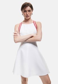 Weißes Kleid mit roten Schulterträgern, A-Linien-Silhouette, glatte Textur und knielanger Saum. Einfaches Design mit minimalen Details.