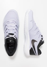 Světlé fialové sportovní boty z síťoviny s černými akcenty a bílými podrážkami. Mají tkaničky a strukturovaný vzorek na podrážce pro lepší přilnavost.